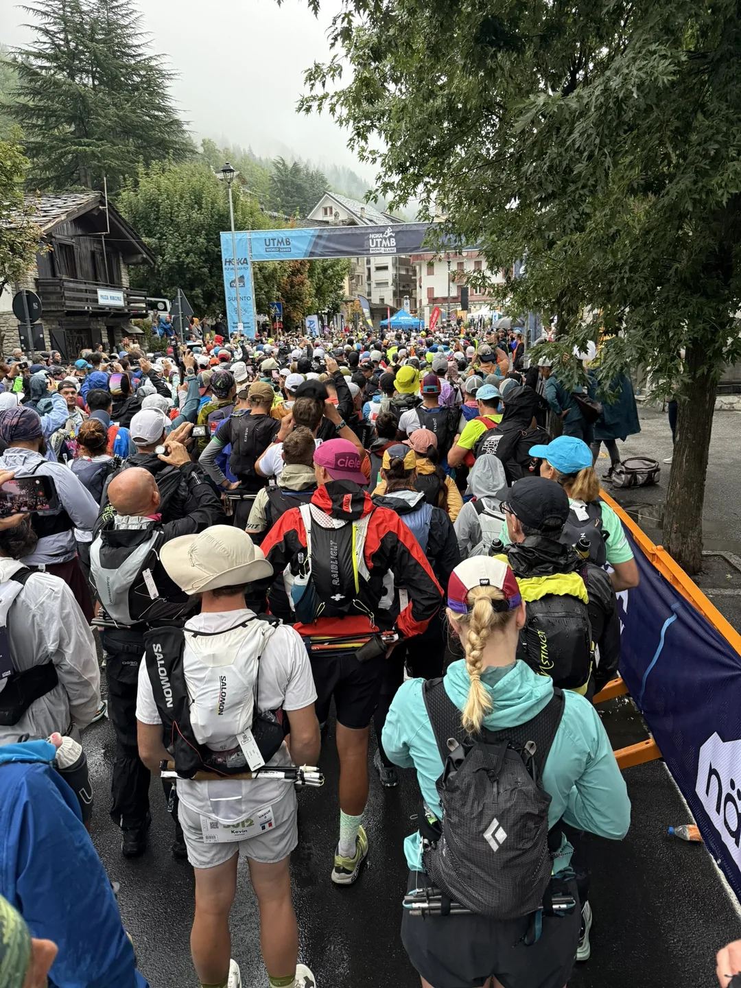 The back of the CCC start pen in Courmayeur under the UTMB arch, packed with runners in the rain.